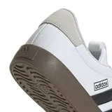 Championes urbanos Adidas modelo VL Court 3.0, con parte superior de cuero sintético blanco, icónicas tres tiras laterales en negro y puntera de gamuza gris. Presenta una suela de caucho vulcanizada en color marrón y cierre de cordones.