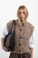 Cartera tipo tote bag de cuero vacuno marrón, con detalles de trenzado artesanal en los laterales y flecos colgantes decorativos. Cuenta con doble asa de hombro y cierre superior.