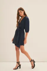 Vestido corto azul marino de manga larga con efecto abullonado en puños, escote cruzado en V y lazo ajustable en la cintura.
