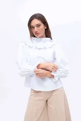 Blusa blanca de algodón con cuello alto fruncido con volados y mangas abullonadas con puños elásticos.