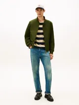 Campera tipo Harrington de Tommy Hilfiger en color verde militar, con cuello alto, cierre frontal de cremallera y bolsillos laterales. Cuenta con elásticos en puños y dobladillo, y el logo bordado en el pecho.