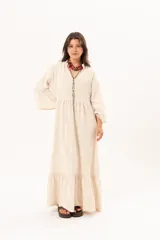 Vestido largo beige de silueta oversize, confeccionado en tela ligera con textura y motivos bordados tono sobre tono. Presenta escote en V, mangas amplias con volados y un gran volado en el ruedo.