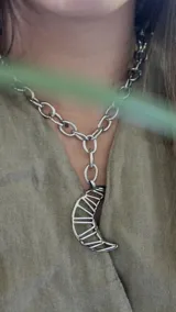 Collar plateado con cadena de eslabones grandes y dije de luna creciente con diseño geométrico calado.
