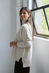 Polerón de cuello alto con diseño de rombos tejidos en relieve, mangas largas con puños acanalados y ruedo asimétrico con aberturas laterales.