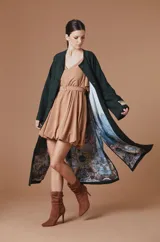 Saco Natalia Antolin de mujer color verde oscuro, de corte largo y diseño relajado con cuello redondo, mangas anchas y cierre frontal de botones oscuros. Incluye una etiqueta decorativa distintiva de la marca en el puño de la manga izquierda.
