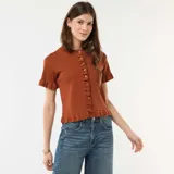 Camiseta de punto color marrón, de manga corta con terminación en volantes, cuello redondo y cierre frontal con botones, decorada con una hilera de volantes a lo largo de la botonadura.