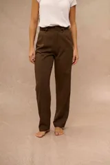 Pantalón de vestir marrón de tiro alto, corte recto y pinzas en la parte delantera. Cuenta con presillas para cinturón y detalles ajustables con hebillas metálicas en los laterales de la cintura.