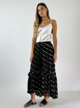 Pollera larga de color negro con estampado de rayas horizontales blancas difuminadas y volados en el ruedo.