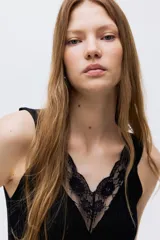 Musculosa entallada de punto acanalado, color negro, con breteles anchos y escote en V profundo decorado con ribete de encaje.