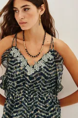 Top de tirantes finos con estampado batik en tonos oscuros y destellos metalizados. Presenta un escote en V decorado con aplicaciones de encaje floral y volados en los laterales.