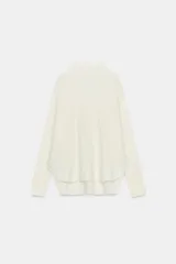 Jersey de punto con textura, color crudo, de cuello subido y manga larga. Presenta un diseño holgado con bajo asimétrico y aberturas laterales.