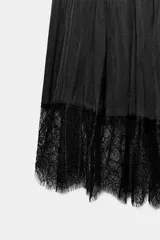 Vestido largo negro de tejido satinado, con escote halter y tirantes finos cruzados en la espalda. Presenta hombros descubiertos y el bajo está acabado con una aplicación de encaje a tono.