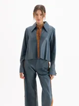 Camisa de cuero ovino color azul, de silueta estructurada, cuello camisero y cierre frontal con broches a presión.