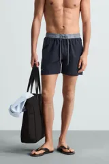 Bañador de hombre azul marino con cintura elástica gris y cordón ajustable. Presenta un pequeño texto estampado en relieve en la parte inferior izquierda.