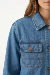 Campera de denim de corte largo, color crudo con costuras en contraste de color marrón, múltiples bolsillos frontales y botones oscuros.