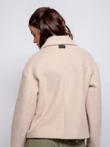 Tapado corto de paño con cuello camisero, cierre frontal de botones veteados y dos bolsillos frontales tipo parche. Presenta un diseño de corte recto y mangas largas.