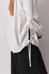 Camisa celeste de calce relajado, con cuello camisero, bolsillo aplicado en el pecho y mangas largas con puños abotonados. Cuenta con lazos ajustables en los laterales para fruncir y regular la silueta.