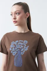 Remera blanca de manga corta con estampado frontal de un florero rojo con rayas verticales y un ramo de flores azules y rojas.