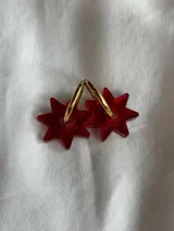 Aros tipo argolla dorada con dije colgante en forma de estrella de acrílico color rosa.