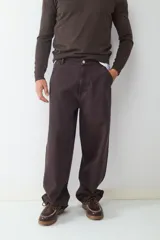 Pantalón estilo skater de corte holgado, color marrón oscuro, con cierre de botón y cremallera, bolsillos laterales y traseros.