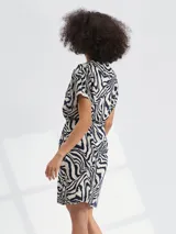 Vestido corto con estampado animal print tipo cebra en tonos blanco y negro. Presenta escote en V, mangas cortas y un lazo ajustable en la cintura para entallar la silueta.