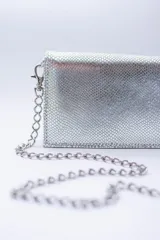Cartera negra con textura símil cocodrilo y cadena metálica plateada.