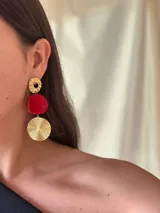 Aros colgantes con tres piezas geométricas: círculo calado dorado, disco rojo y disco dorado con textura de espiral.