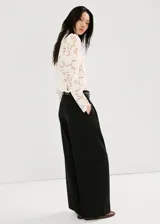 Blusa de encaje blanco con diseño floral, cuello alto y mangas largas con hombreras. Presenta un corte ajustado y acabado delicado.