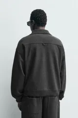Sudadera tipo polo de corte regular, confeccionada en tejido con acabado cepillado. Presenta cuello solapa con cierre frontal de tres botones, manga larga y terminaciones en rib en puños y ruedo.