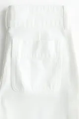 Pantalón jean de denim de algodón rígido, color blanco, de corte wide leg con tiro alto, bolsillos delanteros con ribete trenzado y pliegues marcados.