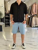 Camisa de manga corta negra con tejido texturizado tipo red, cuello camisero y cierre frontal con botones.