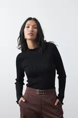 Polera de tejido acanalado color negro, con cuello alto y puños con terminación de volados. Presenta un diseño entallado y textura vertical.