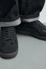 Zapatilla deportiva de estilo retro con diseño de paneles combinados en tonos beige y crema. Presenta detalles en gamuza y una suela de goma en color caramelo.