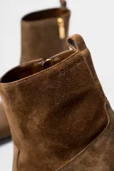Bota corta de estilo western confeccionada en cuero gamuzado color marrón. Presenta un diseño de caña media con tirador trasero, corte asimétrico en el empeine, punta cuadrada y taco bloque de madera.