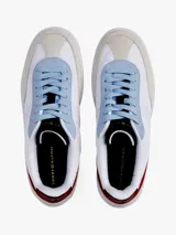 Zapatillas urbanas de corte bajo con exterior de ante blanco, detalles en gris y azul celeste, y refuerzo en el talón de cuero burdeos. Presentan el logo de la marca bordado en el lateral y en la parte trasera.