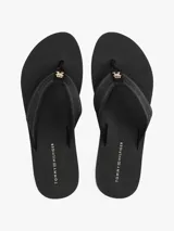 Ojotas negras con suela de EVA y una fina línea blanca decorativa en el borde. Las tiras son de tejido trenzado con inscripción tonal de Tommy Hilfiger y una pequeña insignia metálica con el monograma TH.