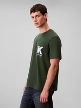 Remera de cuello redondo y manga corta, confeccionada en tejido de punto de algodón. Presenta un estampado frontal con el monograma de Calvin Klein y el logo de la marca en color blanco sobre un fondo verde oscuro.