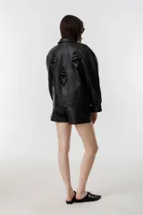 Chaqueta negra de cuero de oveja con apliques tribales en gamuza de cabra al tono, forro capitoneado de poliéster, cuello camisero redondeado, bolsillos frontales, bolsillo interno y botones metálicos a presión forrados.