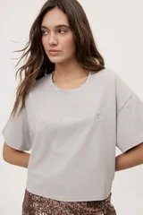 Remera gris de fit amplio, con mangas cortas y cuello redondo. Presenta efecto lavado y estampa frontal con aplicación de strass con la frase "fiesta mode on".