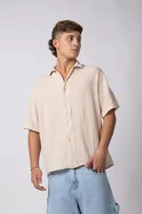 Camisa de hombre de manga corta color beige claro, confeccionada en lino. Tiene cuello clásico, cierre frontal con botones y corte recto.