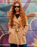 Campera tipo trench de color habano, de corte a la cadera, confeccionada en material textil símil gamuza. Presenta solapa cruzada, doble botonadura frontal, hombreras y cinturón ajustable para anudar en la cintura. Incluye bolsillos delanteros y puños con trabilla.