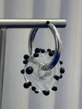Aros tipo argolla con dije de vidrio en forma de dona transparente con pequeñas esferas negras decorativas, montados sobre base de plata 925.