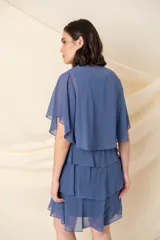 Vestido corto de gasa en color azul, compuesto por un vestido sin mangas con escote redondo decorado con pedrería y una capa corta superpuesta con mangas anchas y diseño en capas escalonadas.