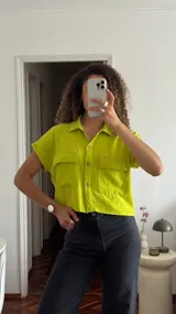 Camisa corta color verde lima, con cuello clásico, cierre frontal con botones y dos bolsillos delanteros con solapa. Presenta mangas cortas y hombros ligeramente caídos con corte recto.