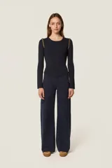 Sweater de punto fino color negro, con cuello redondo y mangas largas. Presenta un diseño ajustado con un corte asimétrico en el ruedo delantero y detalles de cuentas doradas en las costuras de los hombros.