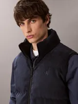 Chaleco acolchado reversible Calvin Klein, con diseño sin mangas, cuello alto y cierre frontal de cremallera. Presenta un lado de pana y otro de nailon liso.