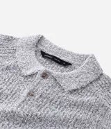 Suéter de punto texturizado color gris claro, con cuello polo y cierre frontal de botones. Presenta mangas largas con puños ajustados y un diseño de corte clásico.