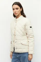 Campera capitoneada color beige, de cuello alto, con bolsillos de solapa y botones metálicos.