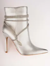Botines plateados con terminación en punta y taco aguja. Decorados con tiras de strass que se enrollan alrededor del tobillo y se atan en el empeine.