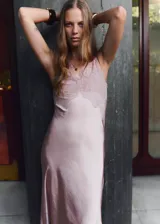 Vestido largo de estilo lencero en tejido satinado color rosado. Presenta escote en pico con detalle de encaje en el pecho y en el bajo, tirantes anchos ajustables y cierre de cremallera lateral.